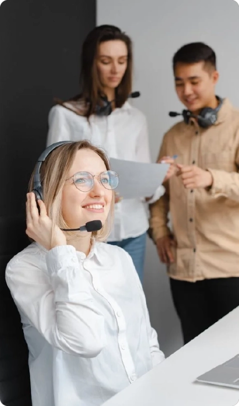 A woman smiling while working at a computer, wearing a headset as a project management virtual assistant
