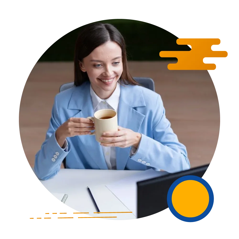 A professional woman in a business suit is seated at her desk, enjoying a cup of coffee while working