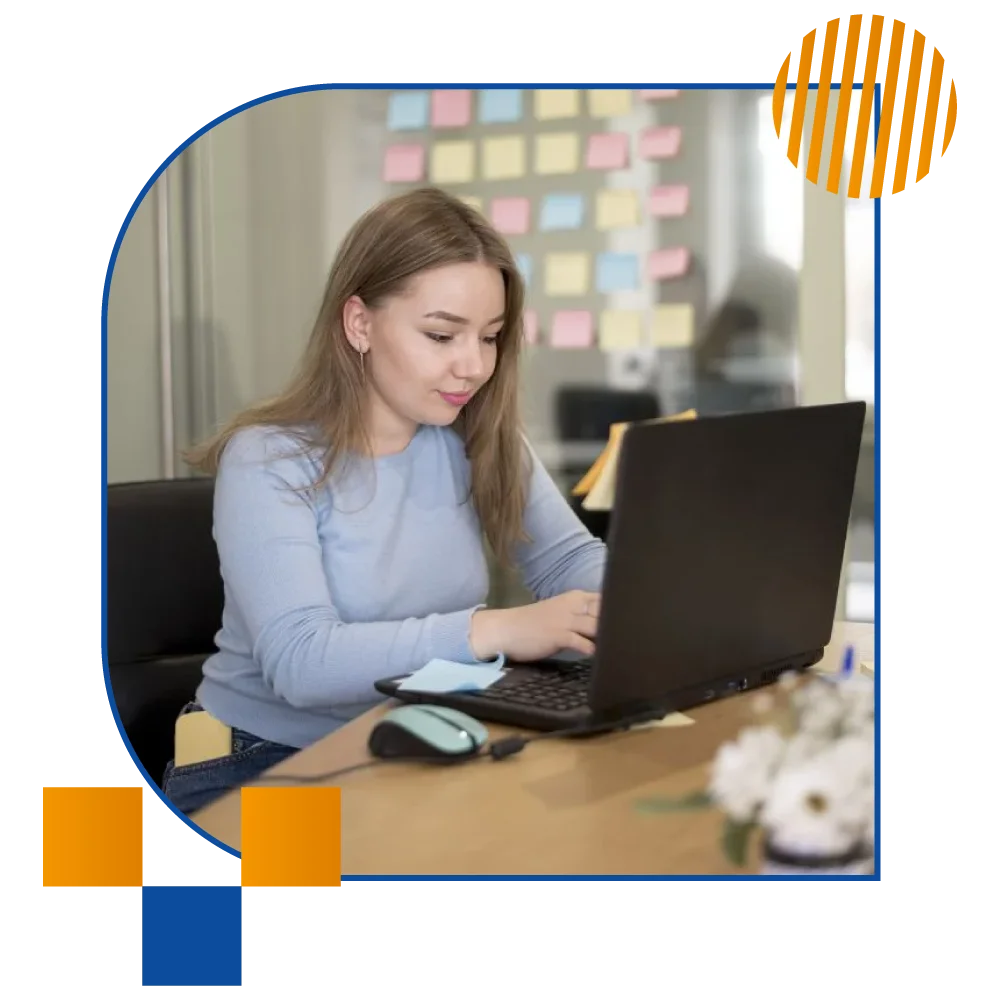 A woman focused on her laptop, seated at a desk in a modern office environment, surrounded by office supplies