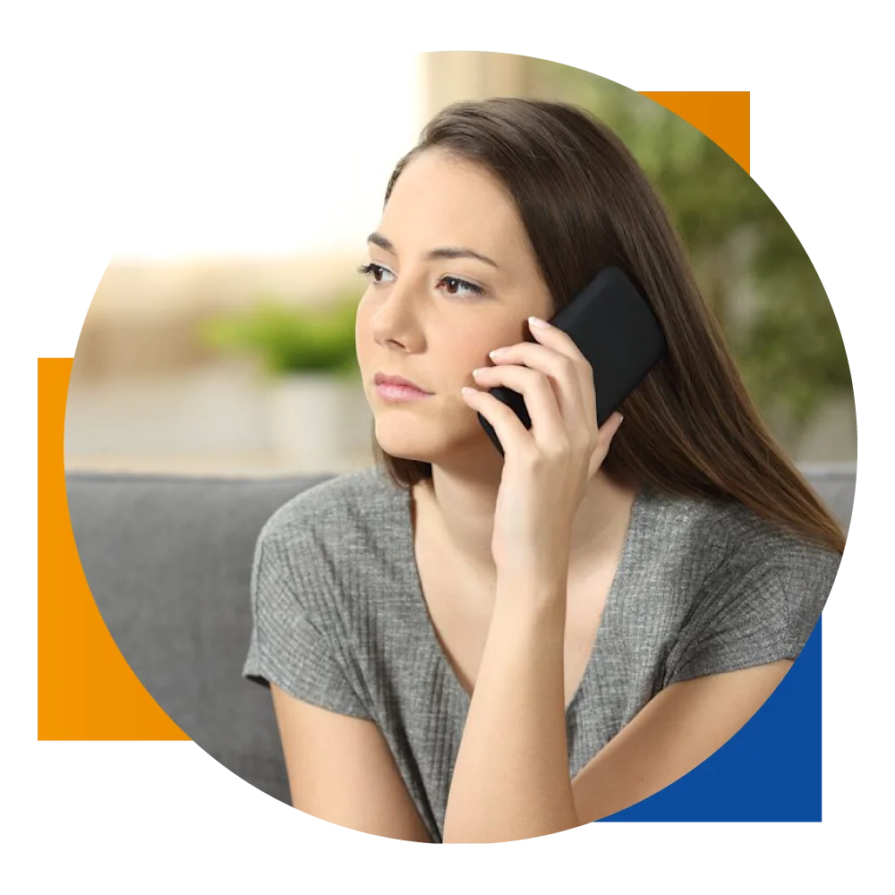 A woman sitting on a couch, engaged in a phone conversation with a focused expression